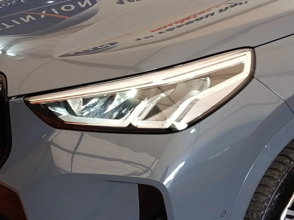 Gros plan sur le phare avant droit d’un BMW X1 xDrive25e M Sport gris foncé 2024 avec peinture métallisée.
