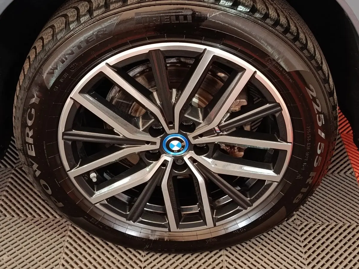 Gros plan sur la jante alliage bicolore noire et argentée avec logo BMW bleu au centre du BMW X1 gris foncé.