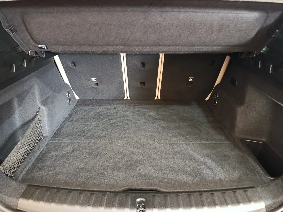 Coffre spacieux ouvert de BMW X1 xDrive25e M Sport gris foncé, avec tapis et filet de rangement latéral visible.