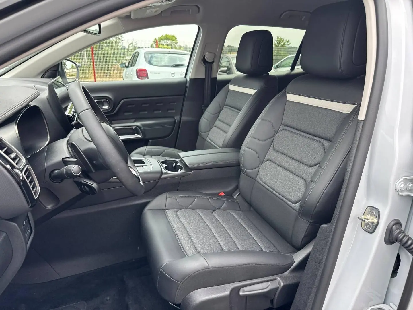 Vue intérieure côté conducteur du Citroën C5 Aircross blanc, sièges avant en tissu et cuir noir avec accoudoir central.