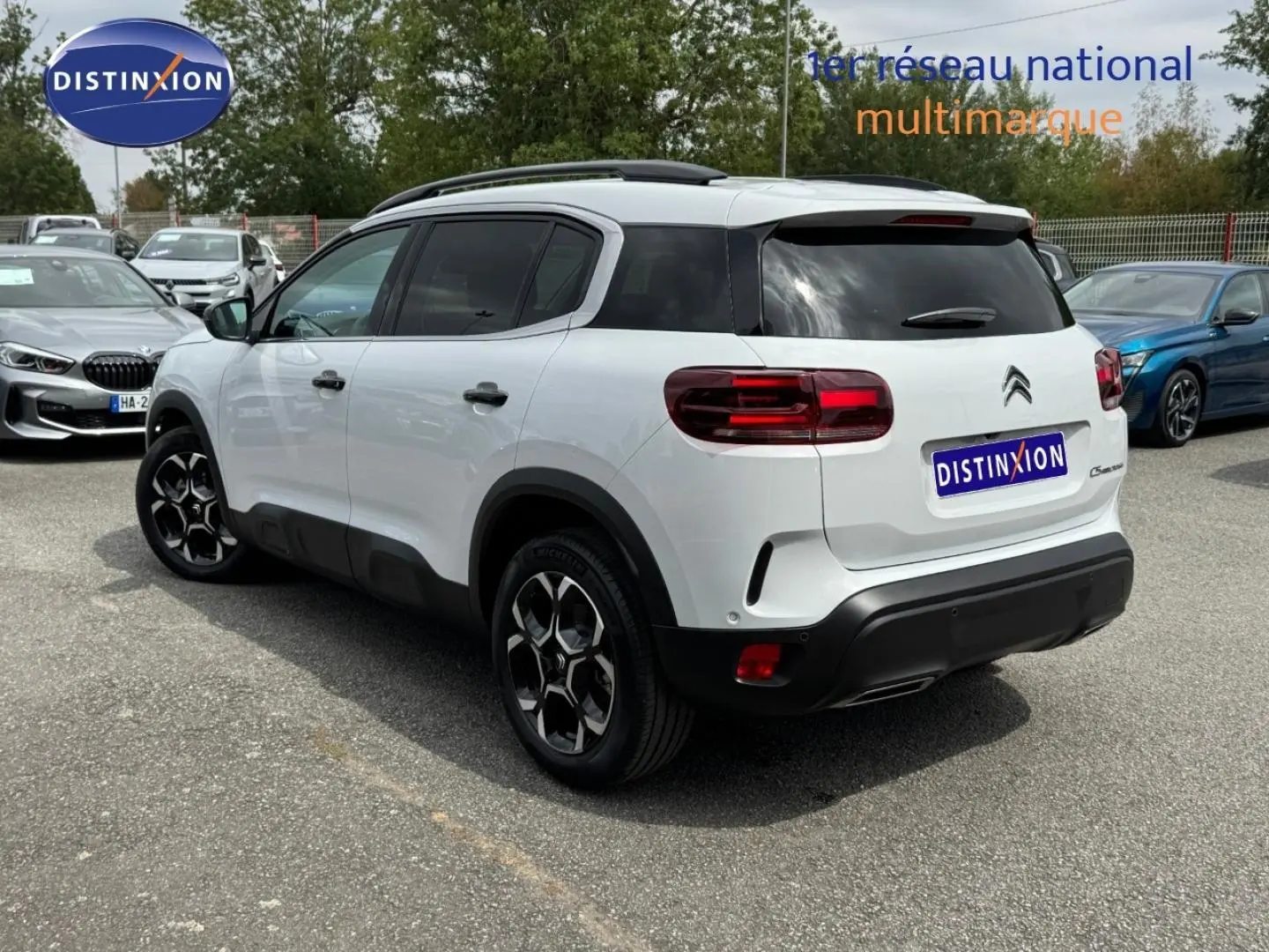 Vue 3/4 arrière droite d'un Citroën C5 Aircross blanc Okénite avec jantes alu et barres de toit noires.