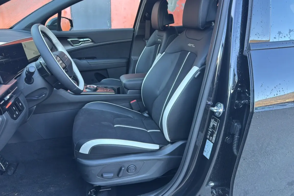 Intérieur côté conducteur du KIA Sportage noir étoilé 2026, sièges sport noirs avec surpiqûres blanches et volant cuir multifonctions.