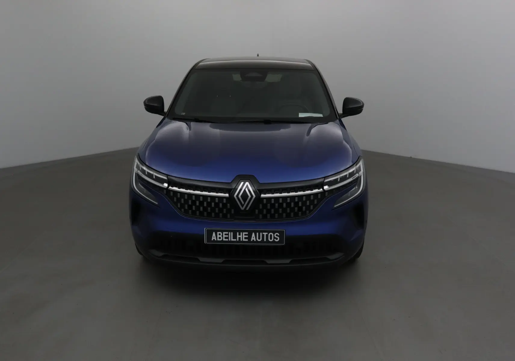 Vue frontale d'un Renault Austral bleu iron avec toit noir, mettant en valeur sa calandre moderne et ses phares LED fins.