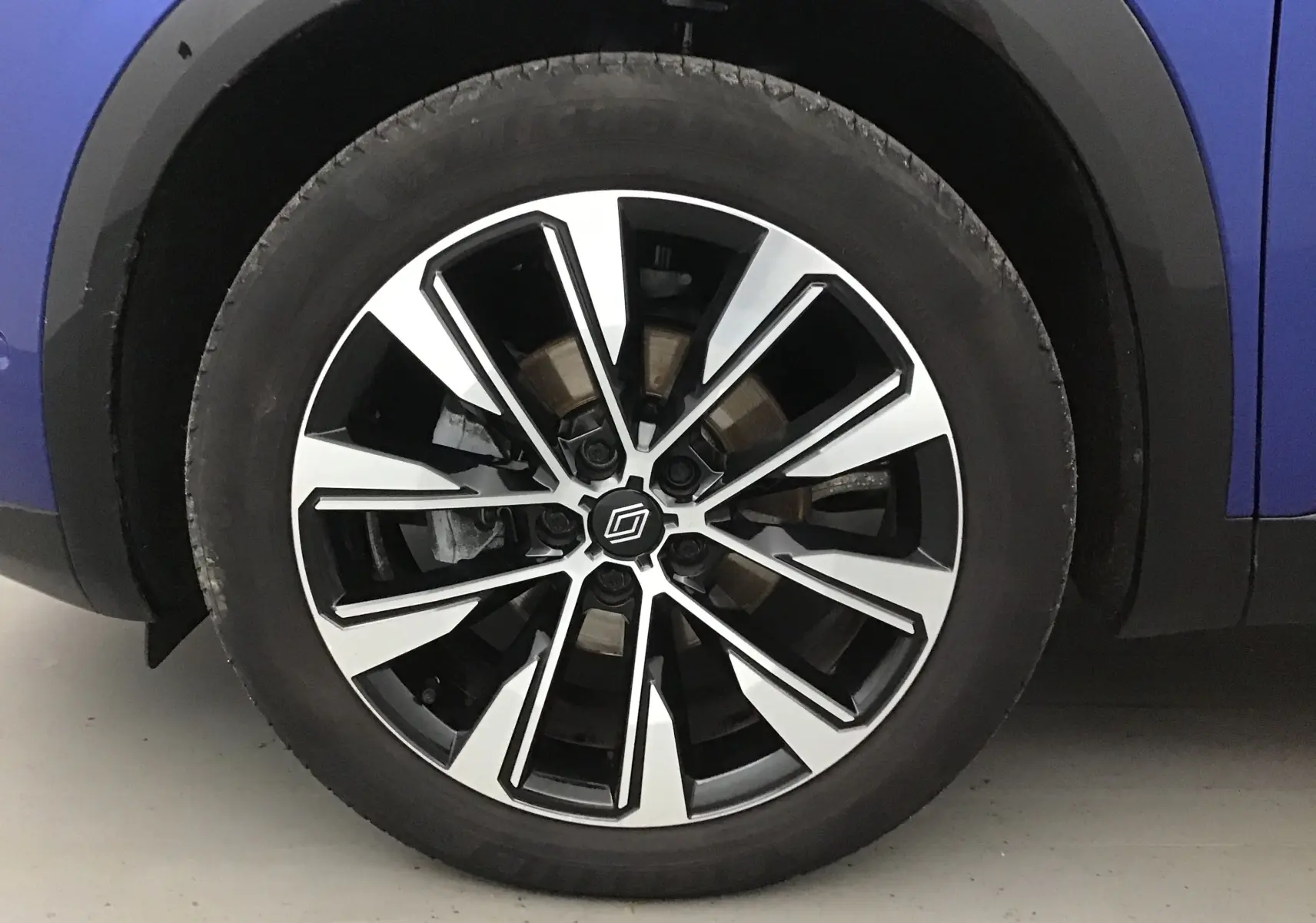 Gros plan sur la roue avant droite du Renault Austral bleu iron avec jante alliage bicolore moderne.