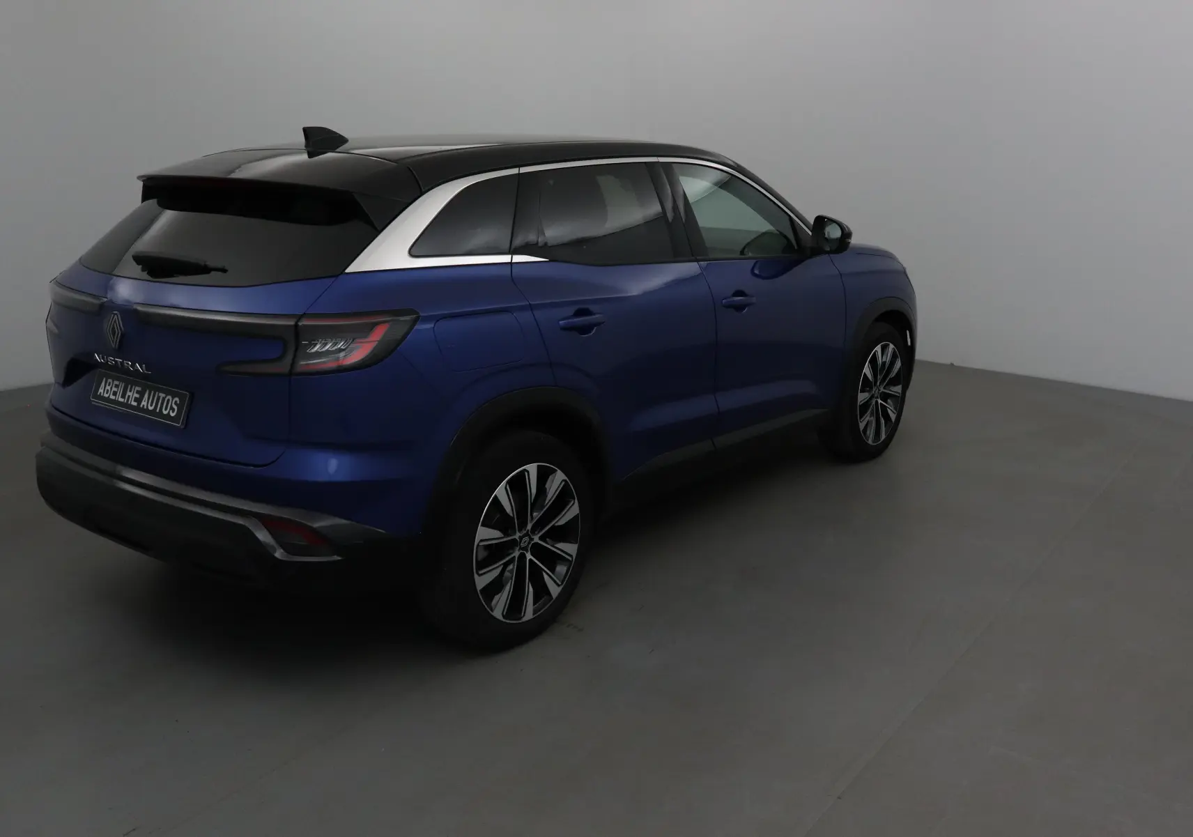 Vue 3/4 arrière droite du Renault Austral bleu Iron avec toit noir et jantes alliage 19 pouces dans un studio.