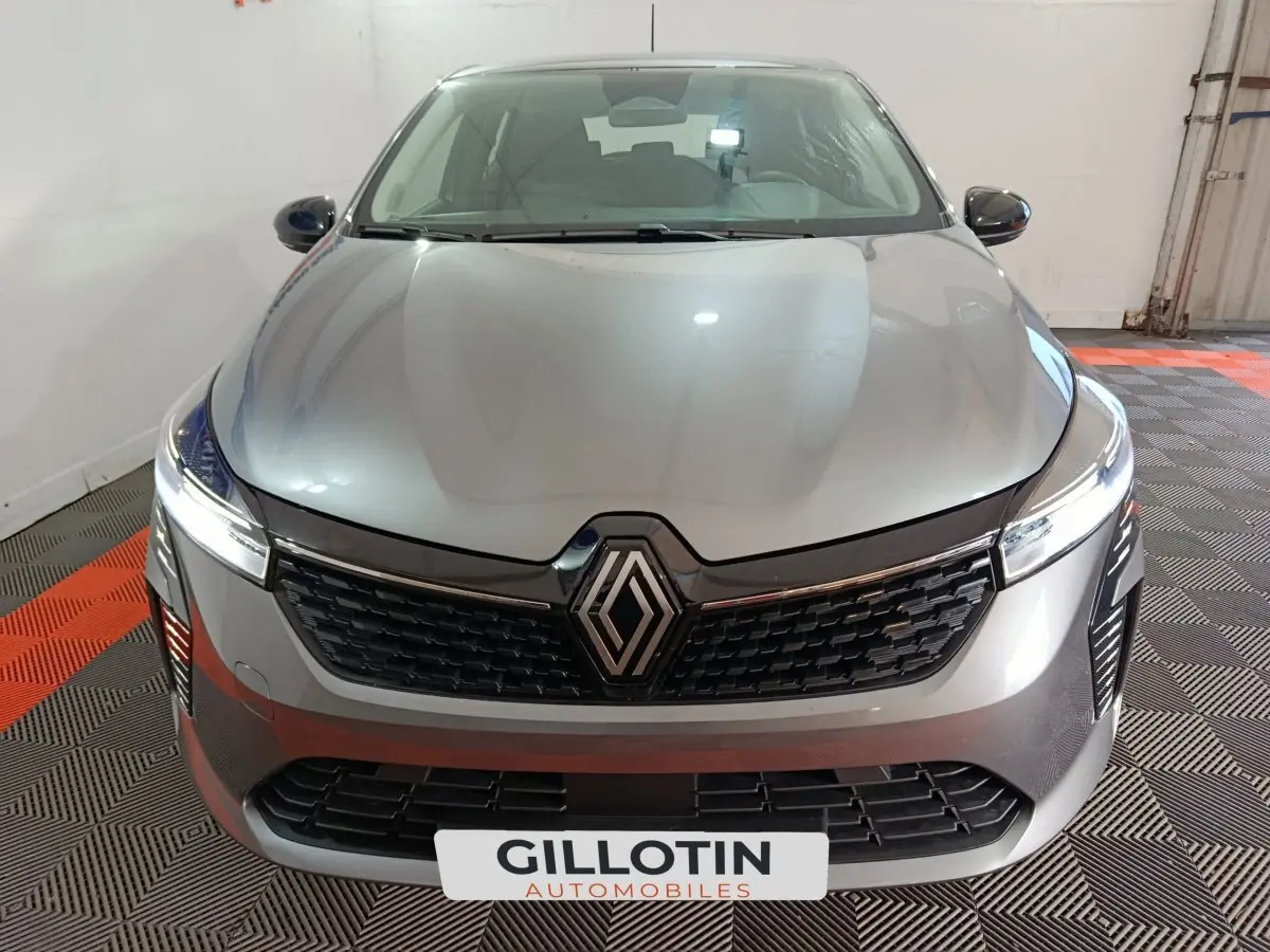 Vue frontale d'une Renault Clio gris foncé avec calandre noire et phares LED allumés dans un garage.