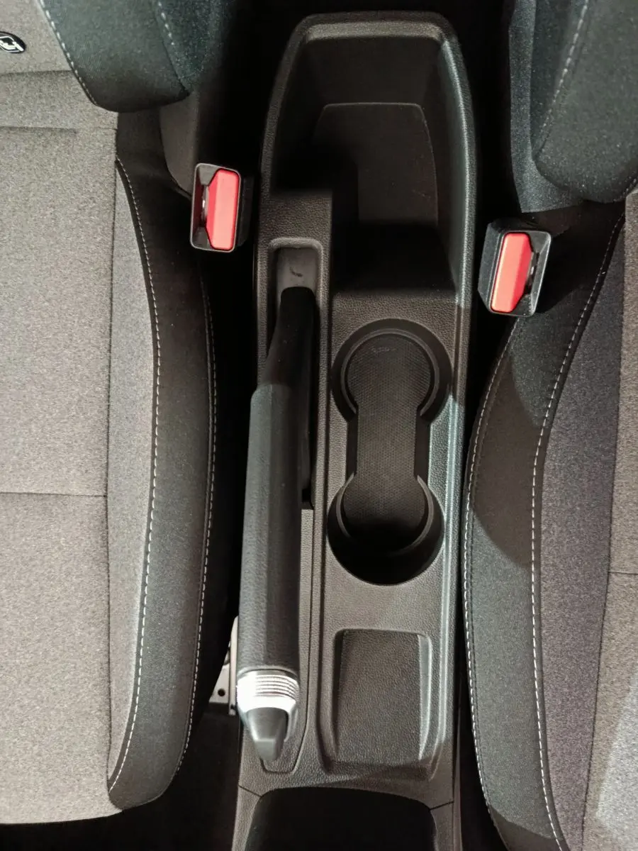 Vue plongeante sur la console centrale noire et les sièges gris foncé de la Renault Clio Evolution 2025 avec frein à main manuel.