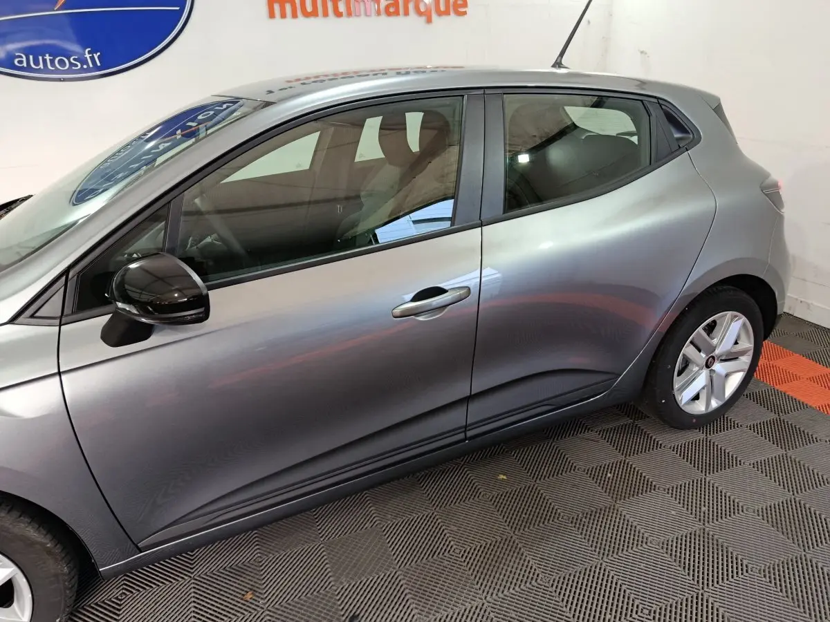 Profil côté gauche d'une Renault Clio gris foncé 2025 garée en intérieur sur sol à damier noir et orange.