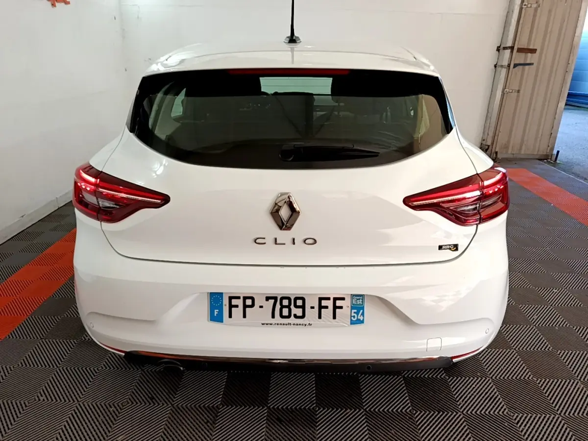 Vue arrière d'une Renault Clio blanche 2020 avec feux LED et logo centré sur un sol à damiers noir et orange.
