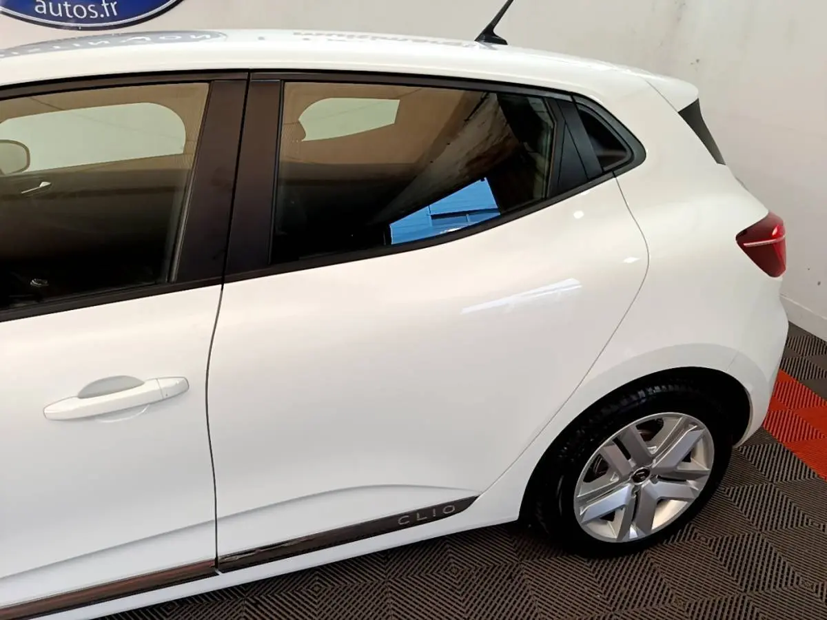 Vue latérale droite d'une Renault Clio blanche avec jante alliage et logo Clio sur la bas de porte.