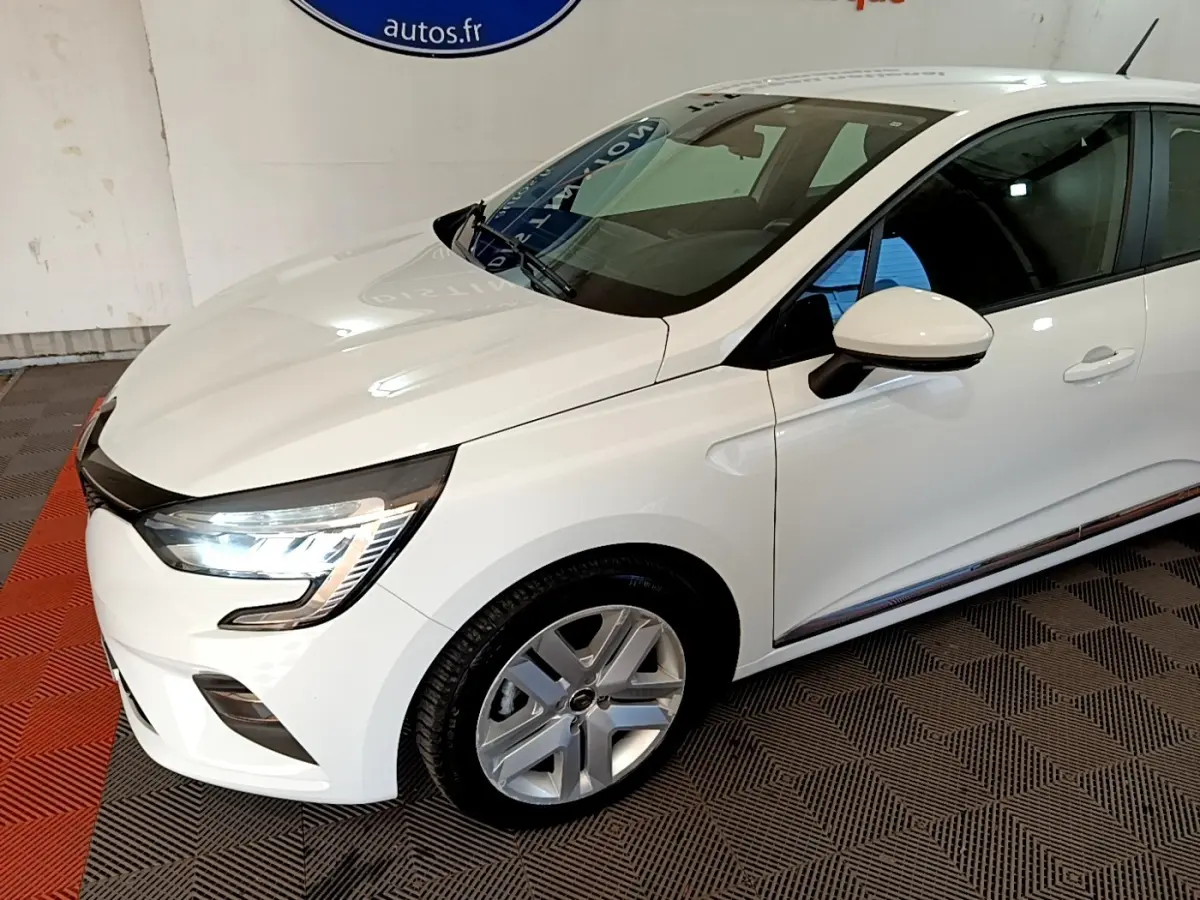 Vue 3/4 avant droite d'une Renault Clio Business Blue dCi 115 blanche avec phares LED allumés et jantes alliage.