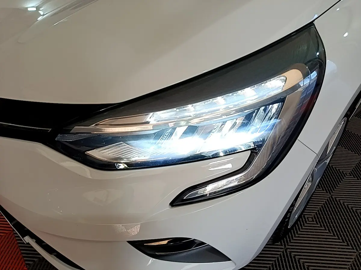 Gros plan sur le phare avant droit allumé d'une Renault Clio Business Blue dCi 115 blanche de 2020.
