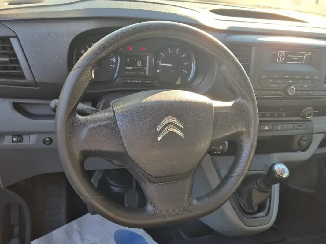 Vue intérieure centrée sur le volant noir et la console centrale du Citroën Jumpy blanc, boîte manuelle visible.