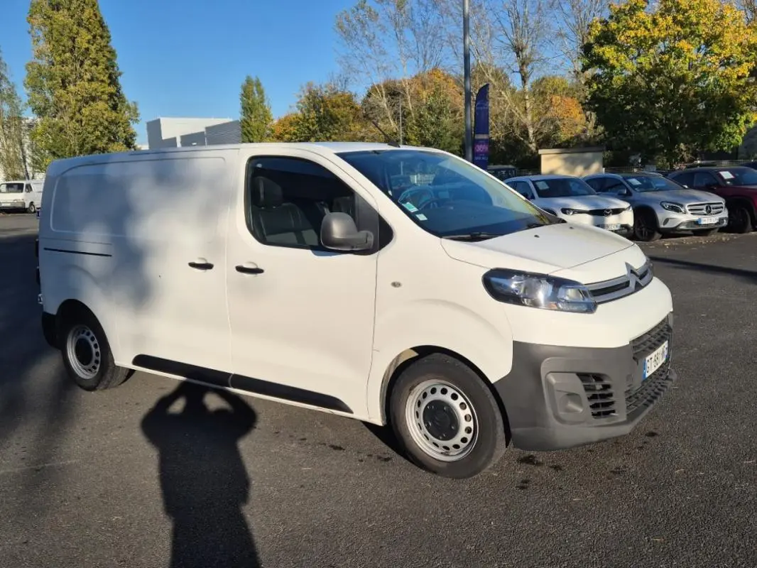 Vue 3/4 avant gauche d’un Citroën Jumpy blanc fourgon L1H1 avec pare-chocs noirs, stationné en extérieur.