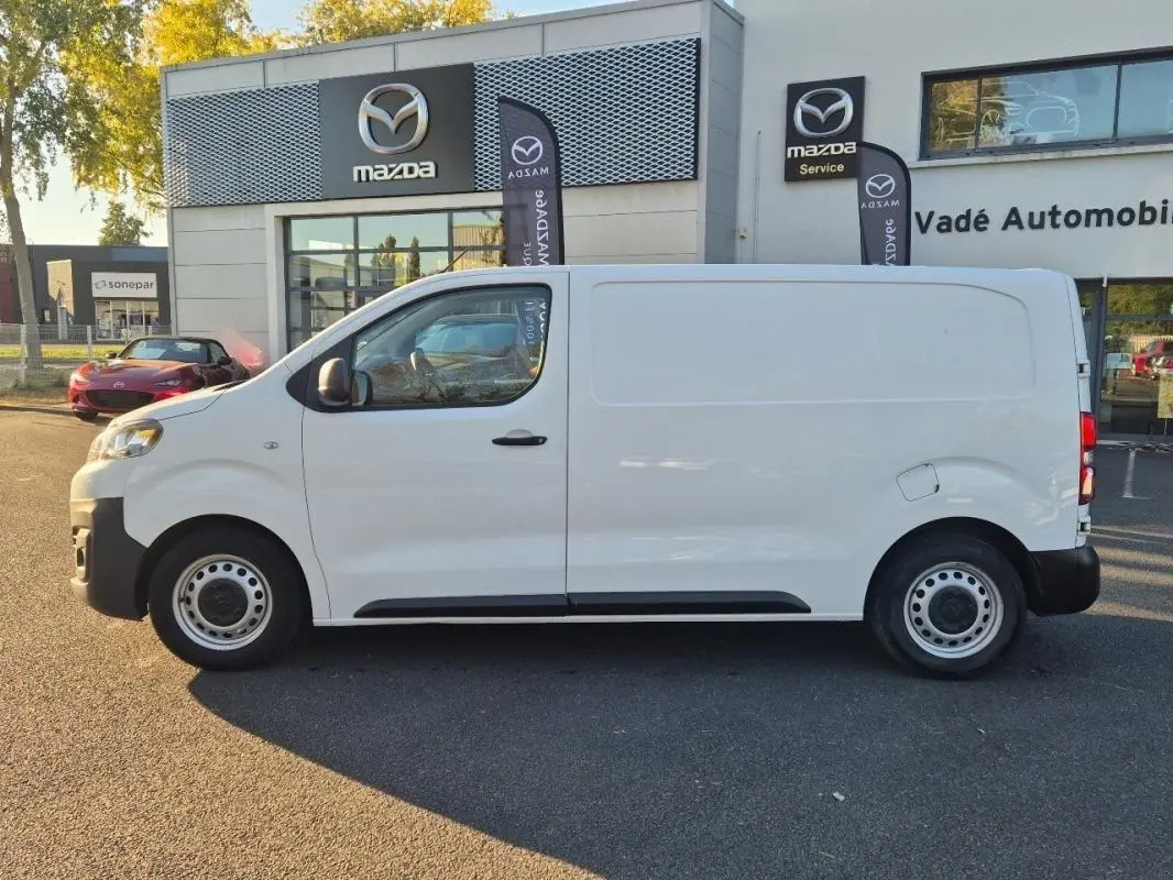 Vue de profil côté gauche d’un fourgon Citroën Jumpy blanc, stationné devant un concessionnaire Mazda.