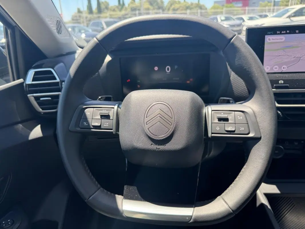Vue frontale du volant cuir noir du Citroën C4 hybride 2025 avec commandes intégrées et tableau de bord numérique.
