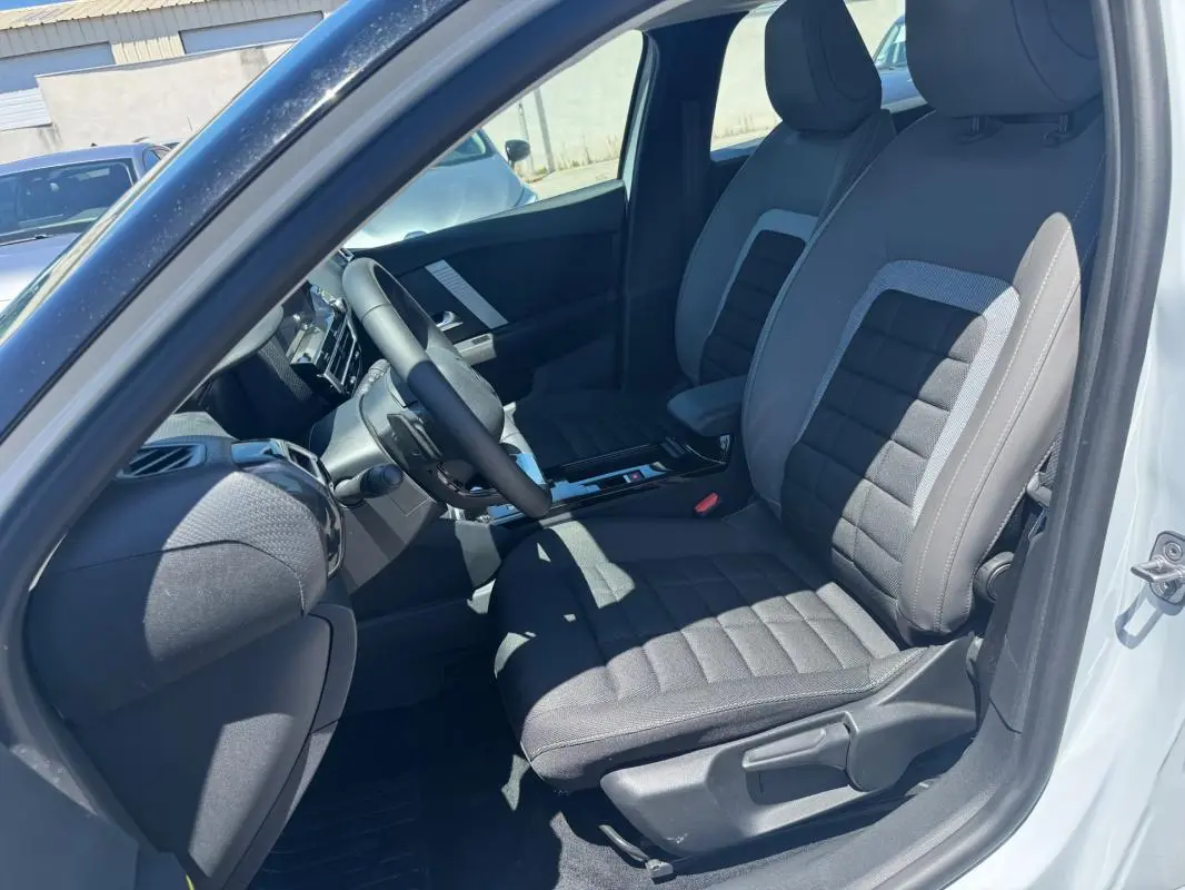 Vue intérieure côté conducteur de la Citroën C4 blanche 2025, montrant sièges tissu et volant cuir.
