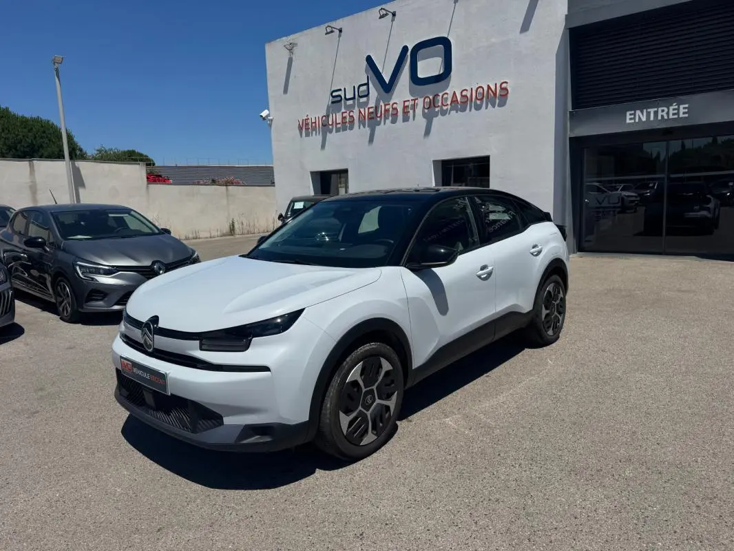 Citroën C4 hybride blanc vue 3/4 avant droit avec toit noir et jantes alliage 18 pouces, stationnée devant un concessionnaire.