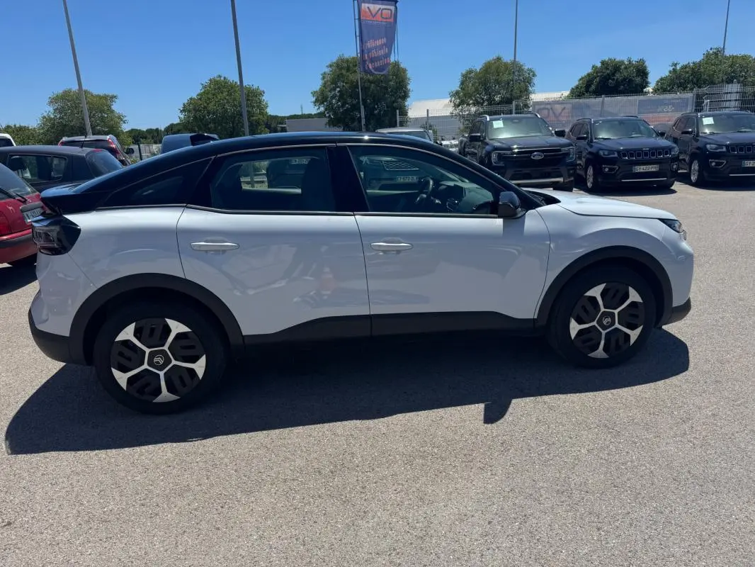 Vue de profil côté gauche d'une Citroën C4 hybride blanche avec toit noir et jantes alliage 18 pouces.