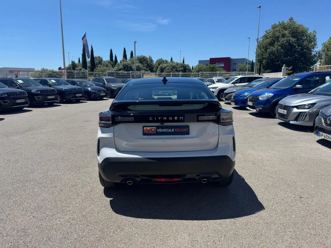Vue arrière d'une Citroën C4 hybride blanche 2025 avec toit noir, feux LED et double sortie d'échappement.