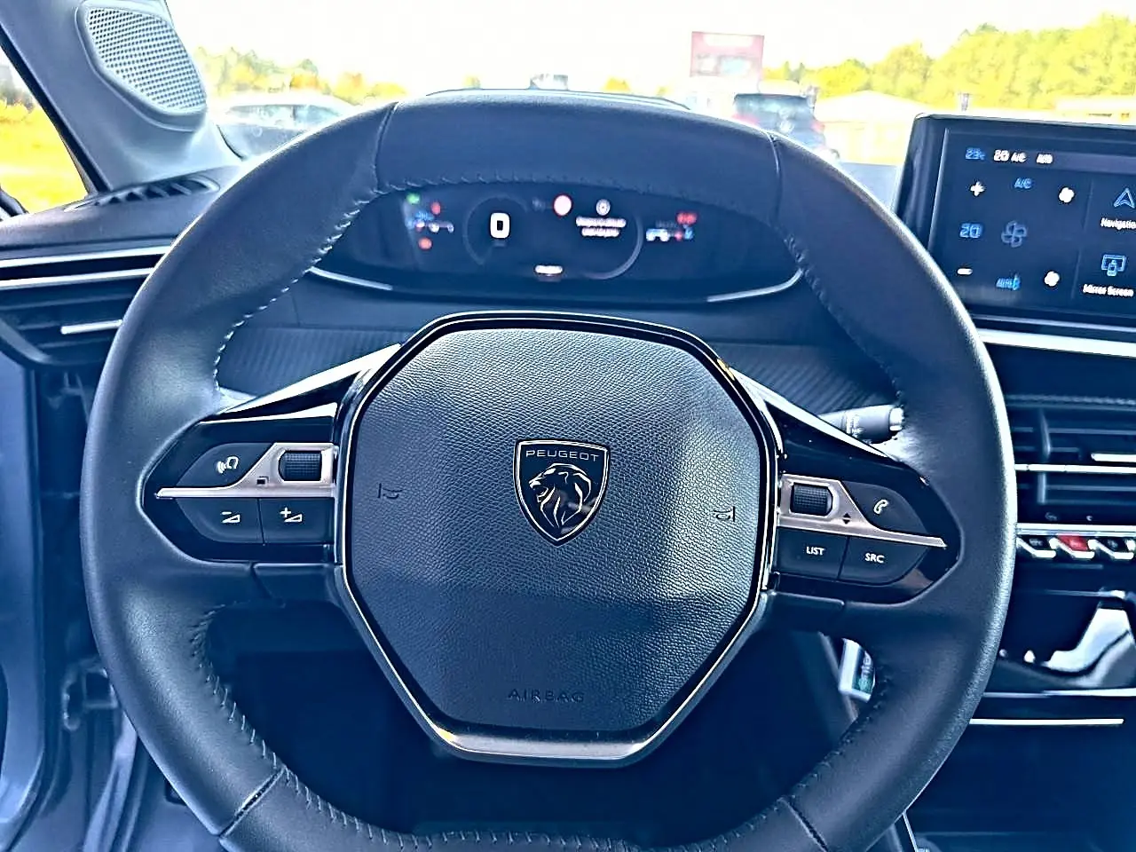 Vue rapprochée du volant cuir noir avec logo Peugeot, tableau de bord numérique et écran tactile du Peugeot 208 1.2 100 Allure.