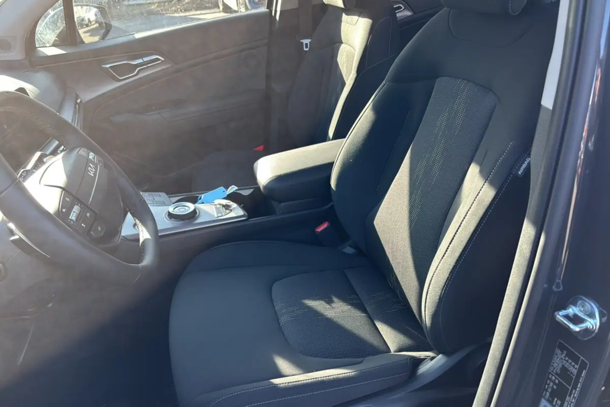 Vue intérieure côté conducteur du Kia Sportage gris eclipse 2026, sièges tissu noirs et volant cuir multifonctions.