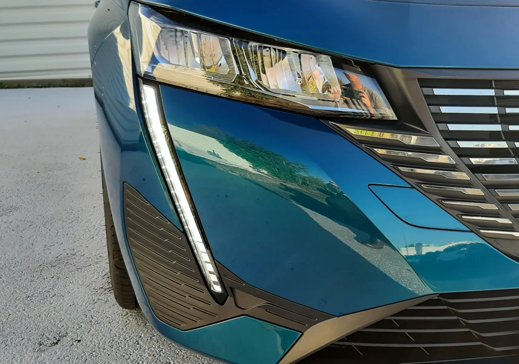 Gros plan sur l'avant droit bleu obsession d'une Peugeot 308 2025, mettant en valeur le phare et la calandre moderne.