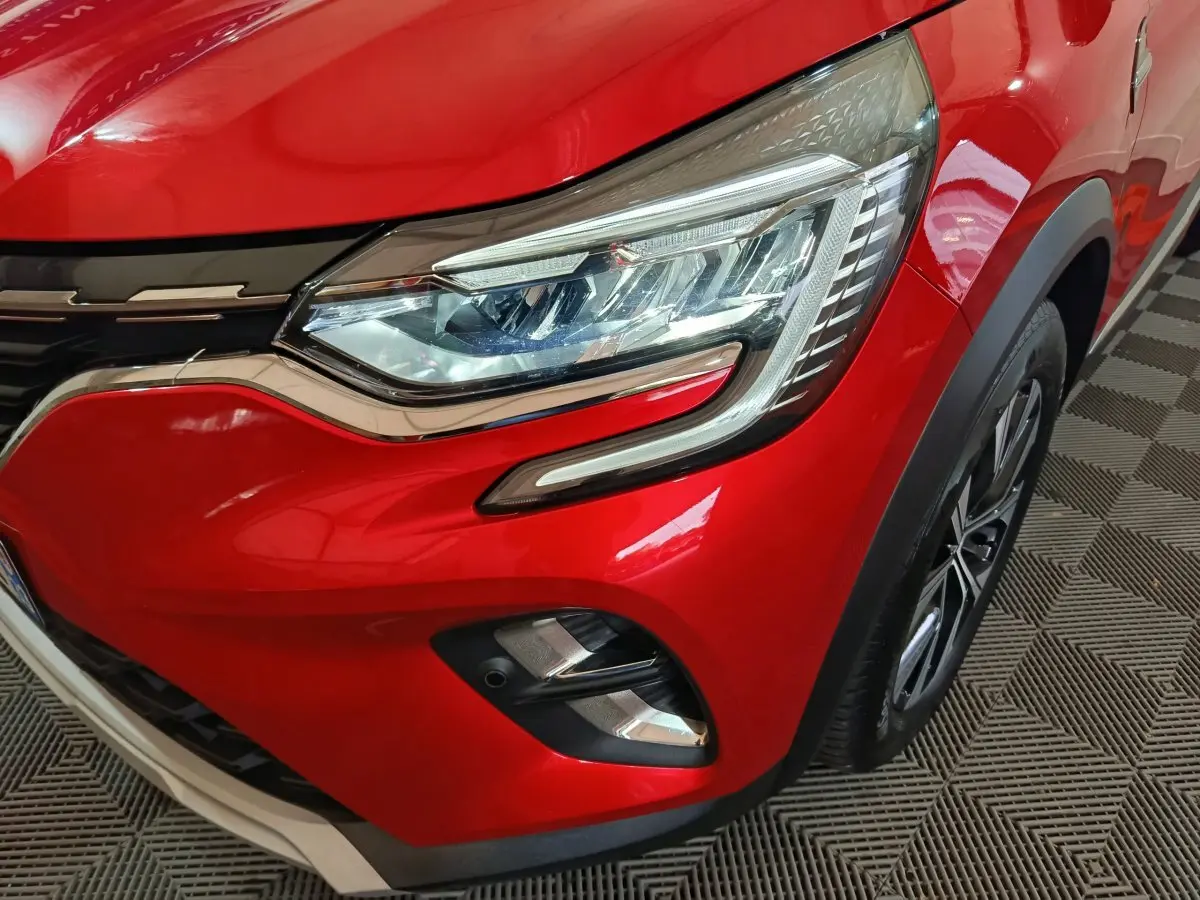 Gros plan sur le phare avant droit du Renault Captur rouge 2024 avec détails chromés et jante visible.