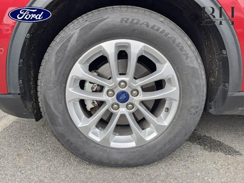 Gros plan sur la roue avant droite du Ford Kuga rouge Premium Lucid avec jante alu et logo Ford au centre