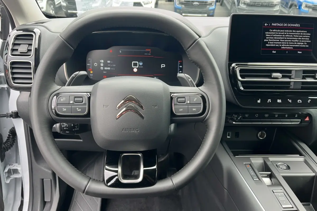 Vue intérieure centrée sur le volant cuir multifonctions et le tableau de bord numérique du Citroën C5 Aircross blanc okénite.