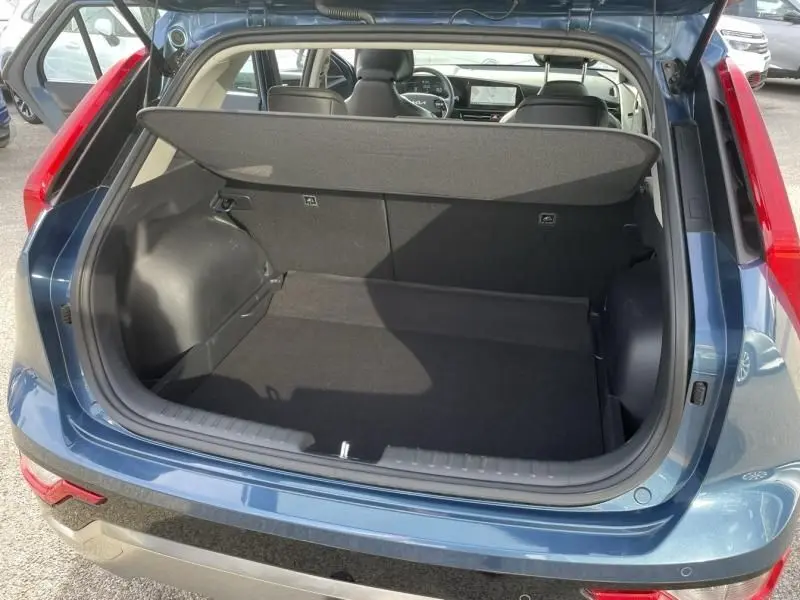 Coffre ouvert vu de l'arrière d'un KIA NIRO 2024 bleu métal, montrant l'espace de chargement et l'intérieur des sièges.