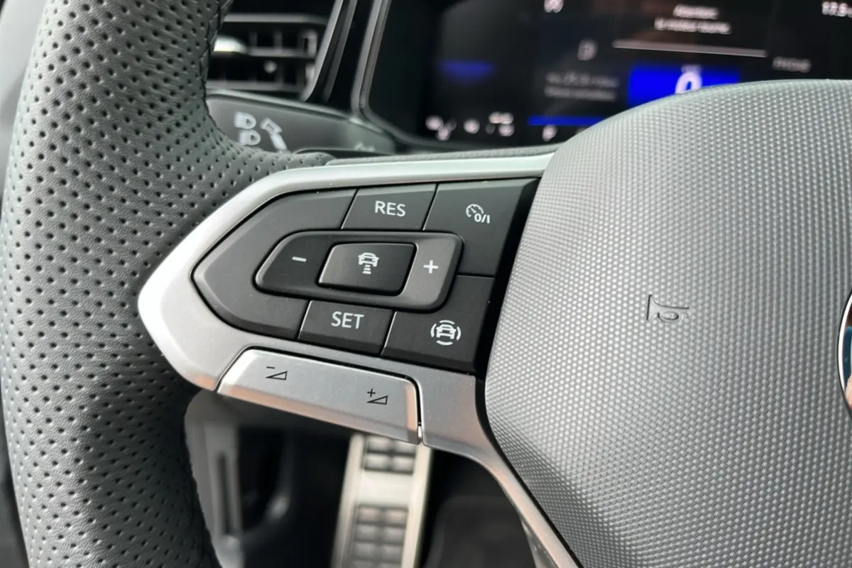 Gros plan sur les commandes de régulateur de vitesse au volant cuir perforé du Volkswagen T-Roc TDI 150 R-Line noir.