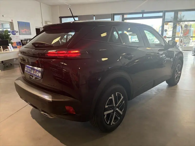 Vue 3/4 arrière droit d’un Peugeot 2008 Hybrid noir métal en showroom, avec feux arrière allumés et jantes alliage.