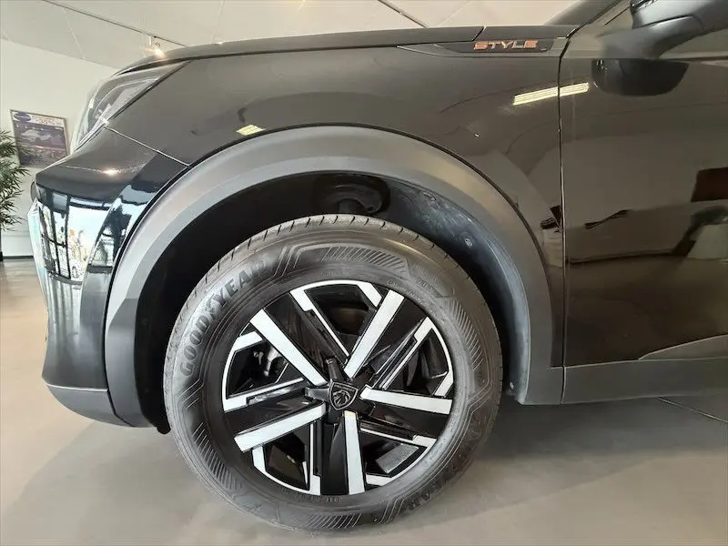 Gros plan sur la roue avant gauche noire métallisée du Peugeot 2008 Hybrid 145ch Style avec jante alu bicolore et badge Style.