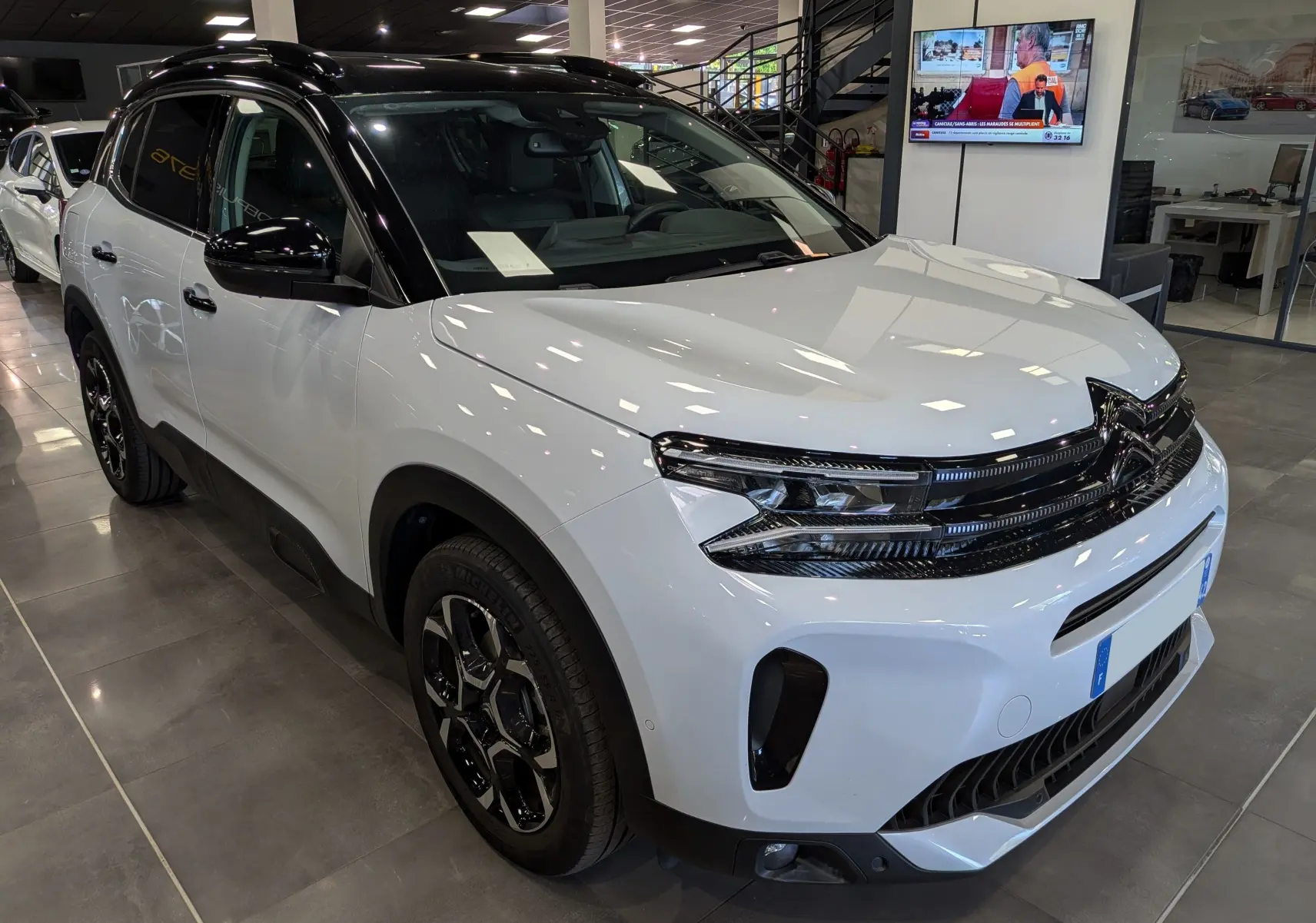Vue 3/4 avant droit du Citroën C5 Aircross 2025 blanc Okénite avec toit noir et jantes noires en concession.