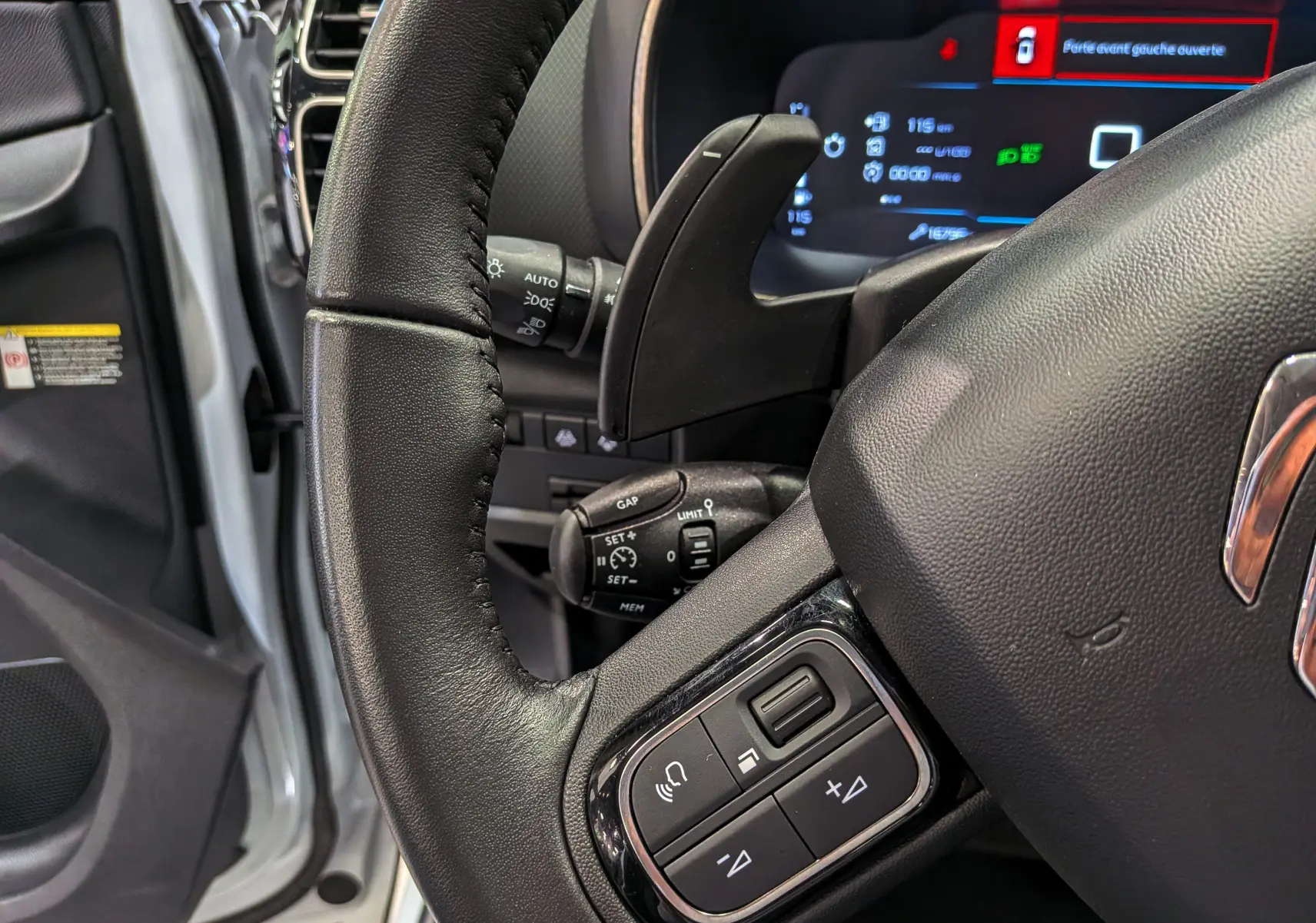 Gros plan sur le volant cuir noir du Citroën C5 Aircross 2025, avec commandes intégrées et porte avant gauche ouverte.