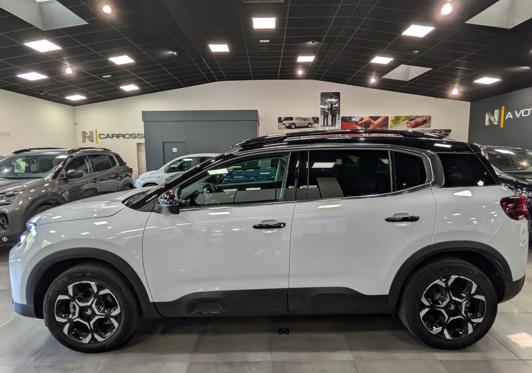 Vue de profil côté gauche d’un Citroën C5 Aircross 2025 blanc Okénite avec toit noir et jantes biton dans un showroom.