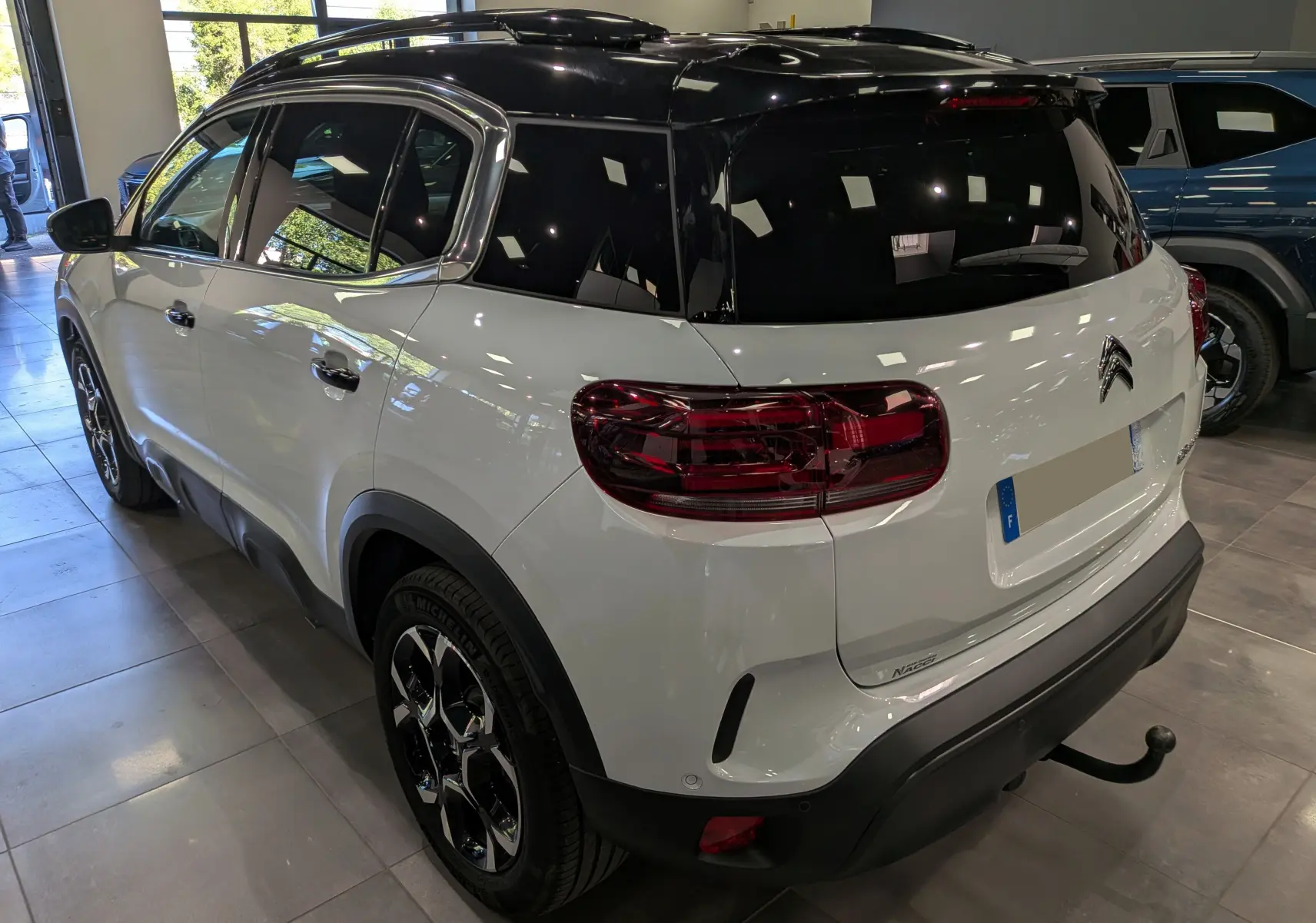 Vue 3/4 arrière droite du Citroën C5 Aircross blanc Okénite avec toit noir et attelage visible en showroom.