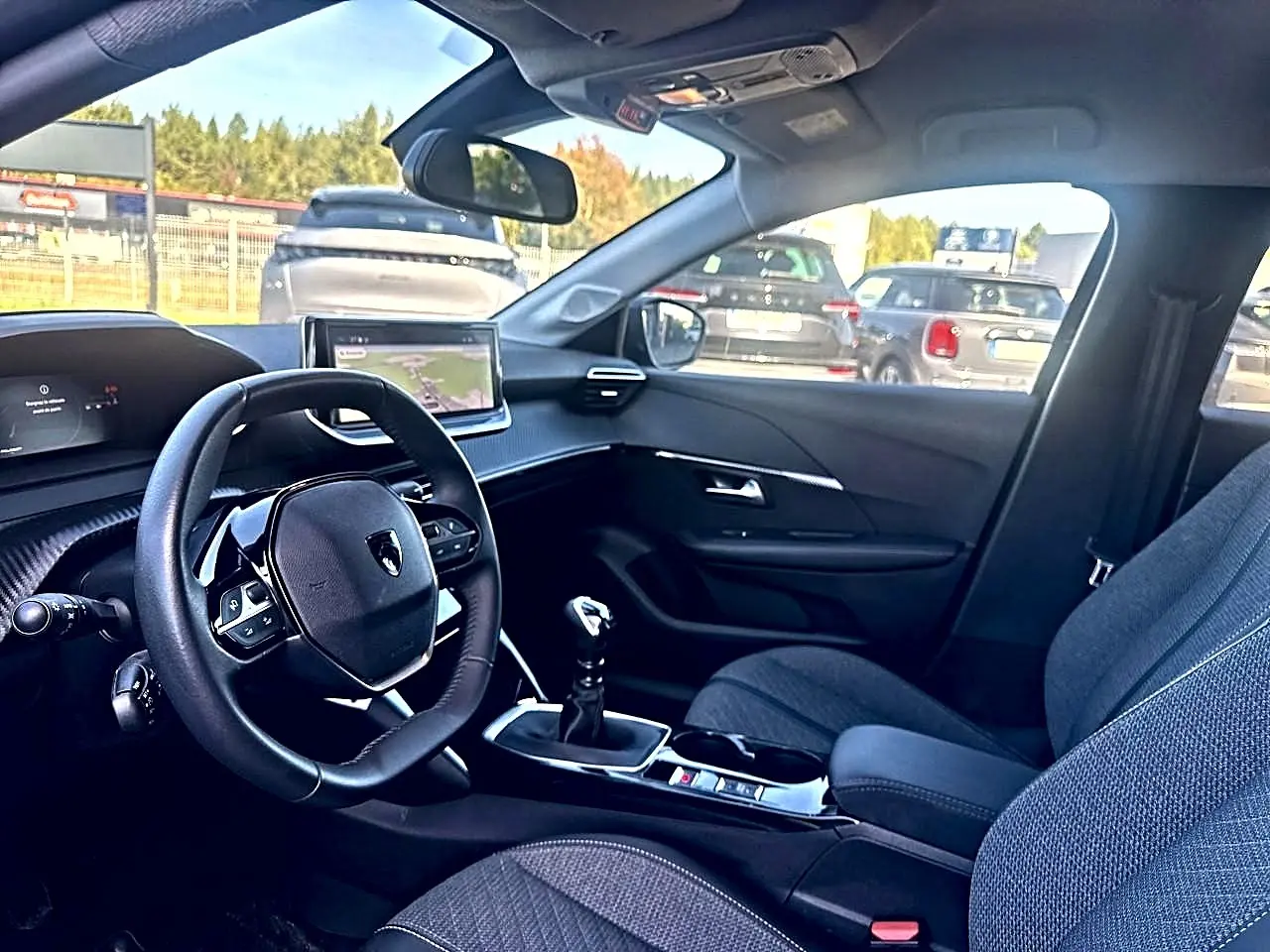 Vue intérieure côté conducteur de la Peugeot 208 noire 2025, montrant le volant, écran tactile et sièges tissu gris.