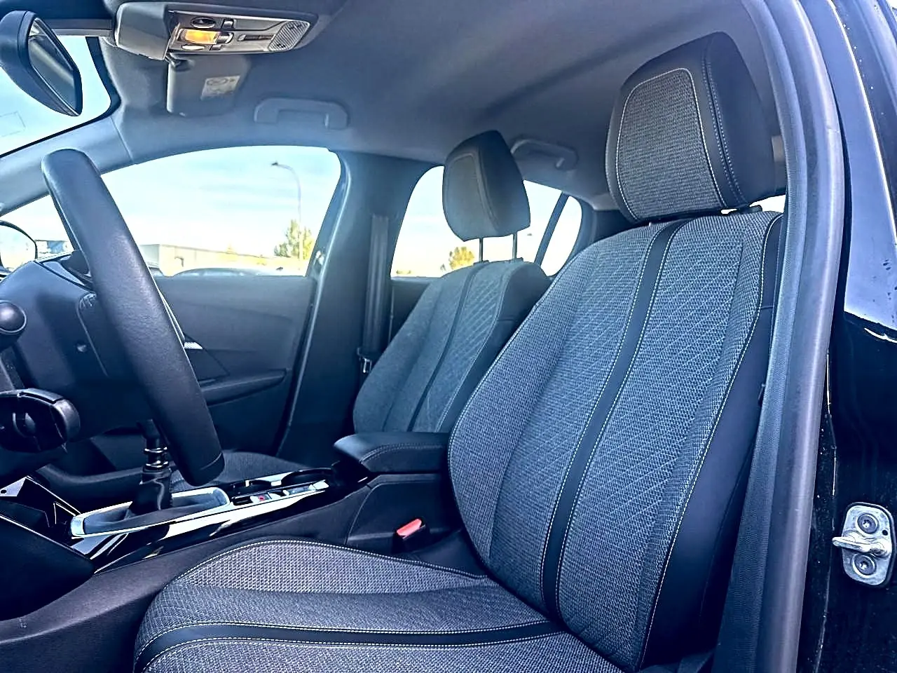 Intérieur de la Peugeot 208 1.2 100 Allure noir, vue côté conducteur sur les sièges en tissu gris et volant.