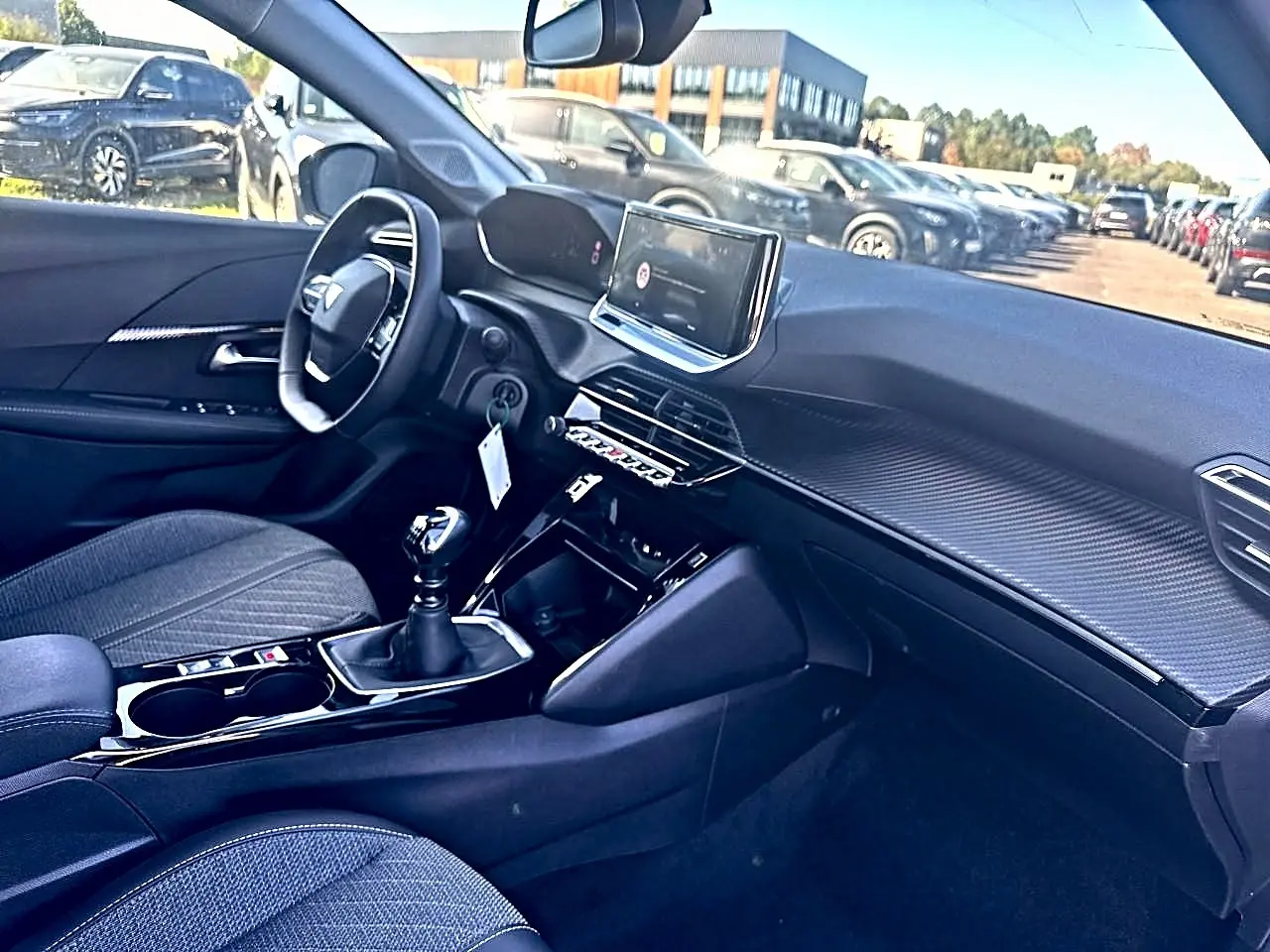 Intérieur de Peugeot 208 1.2 100 allure noir, vue côté conducteur, tableau de bord avec écran tactile et boîte manuelle.