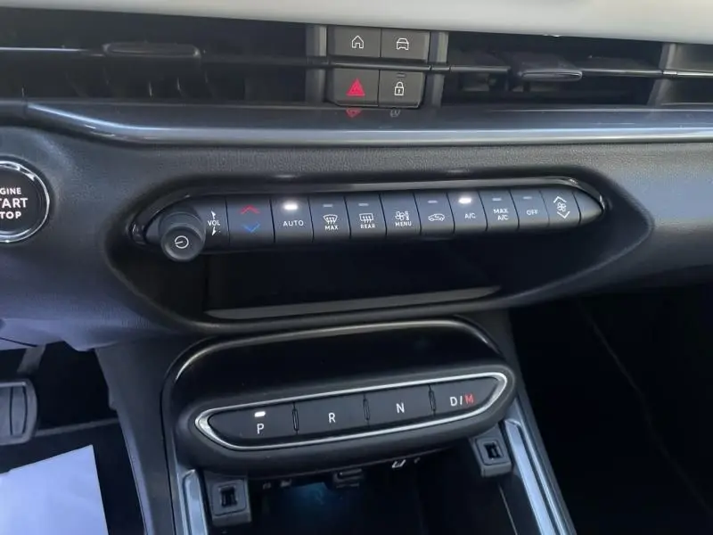 Gros plan sur la console centrale noire du Fiat 600 blanc 2025, montrant les commandes climatisation et la boîte auto à boutons.