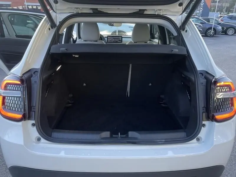 Vue arrière ouverte du coffre d'une FIAT 600 blanche 1.2 Hybrid 2025, avec feux arrière allumés et intérieur noir.