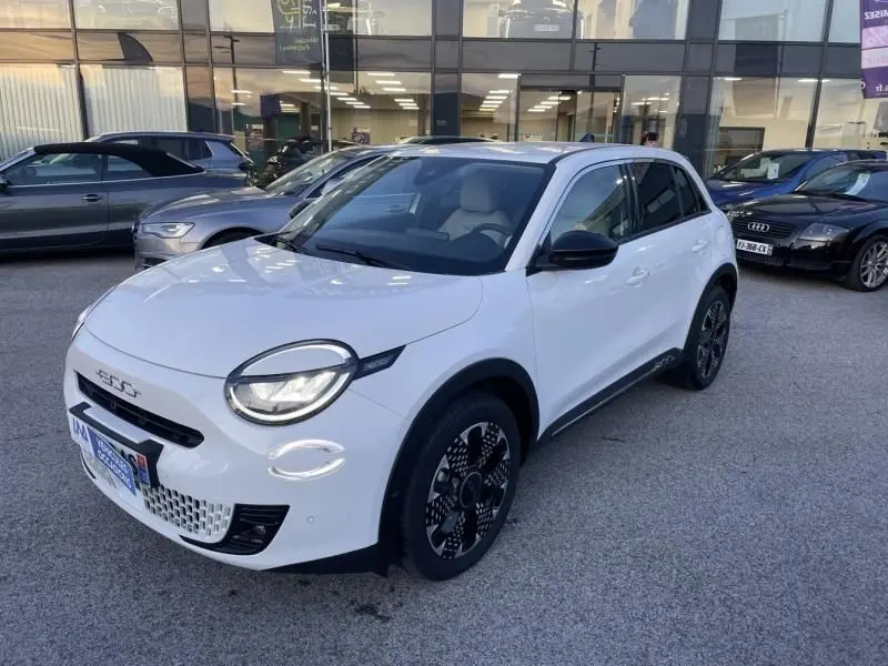 Vue 3/4 avant droite d'une FIAT 600 blanche 2025 avec jantes noires au design graphique et toit noir contrasté.