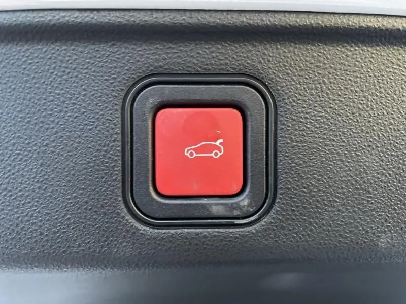 Bouton rouge de déverrouillage du coffre dans l'habitacle d'une FIAT 600 blanche hybride 2025, vue en gros plan.