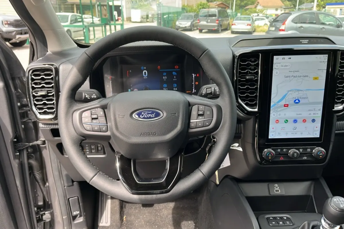 Vue intérieure centrée sur le volant cuir multifonctions et l’écran tactile vertical du Ford Ranger gris carbone 2025.