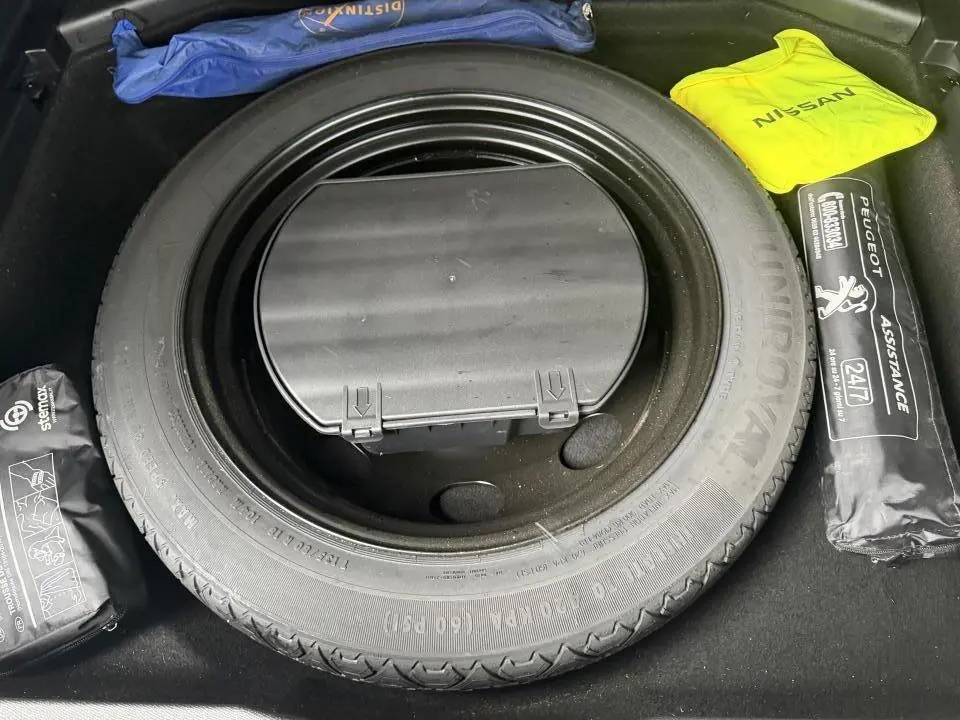 Vue rapprochée de la roue de secours galette dans le coffre d'un Peugeot 3008 blanc avec kit d'assistance et trousse de secours.