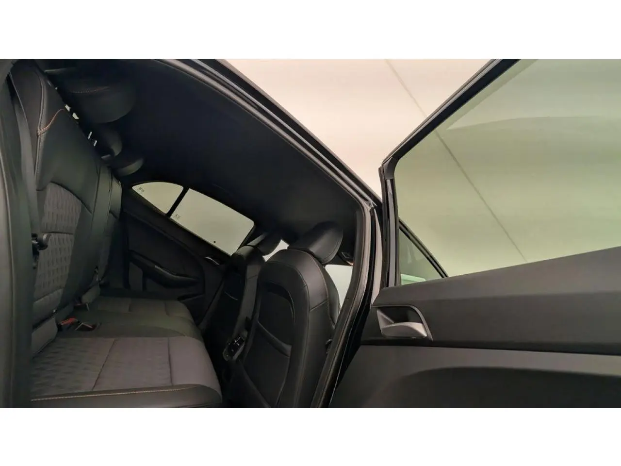 Vue intérieure arrière côté gauche de la MG3 1.5 Hybrid+ 2026 avec sellerie tissu/similicuir noir et porte ouverte.