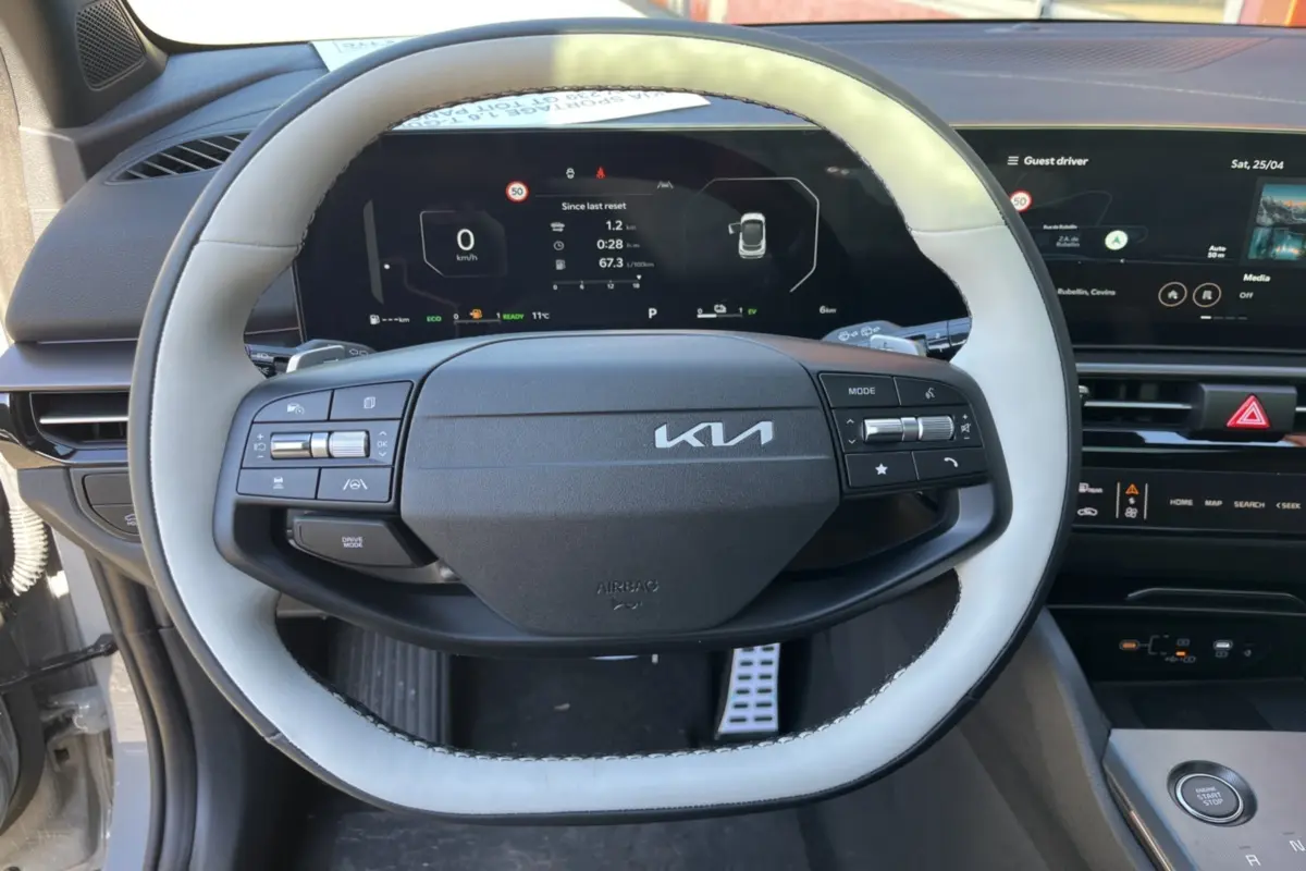 Vue rapprochée du volant cuir gris clair et noir du Kia Sportage 1.6 T-GDI HEV 239 GT avec tableau de bord numérique.