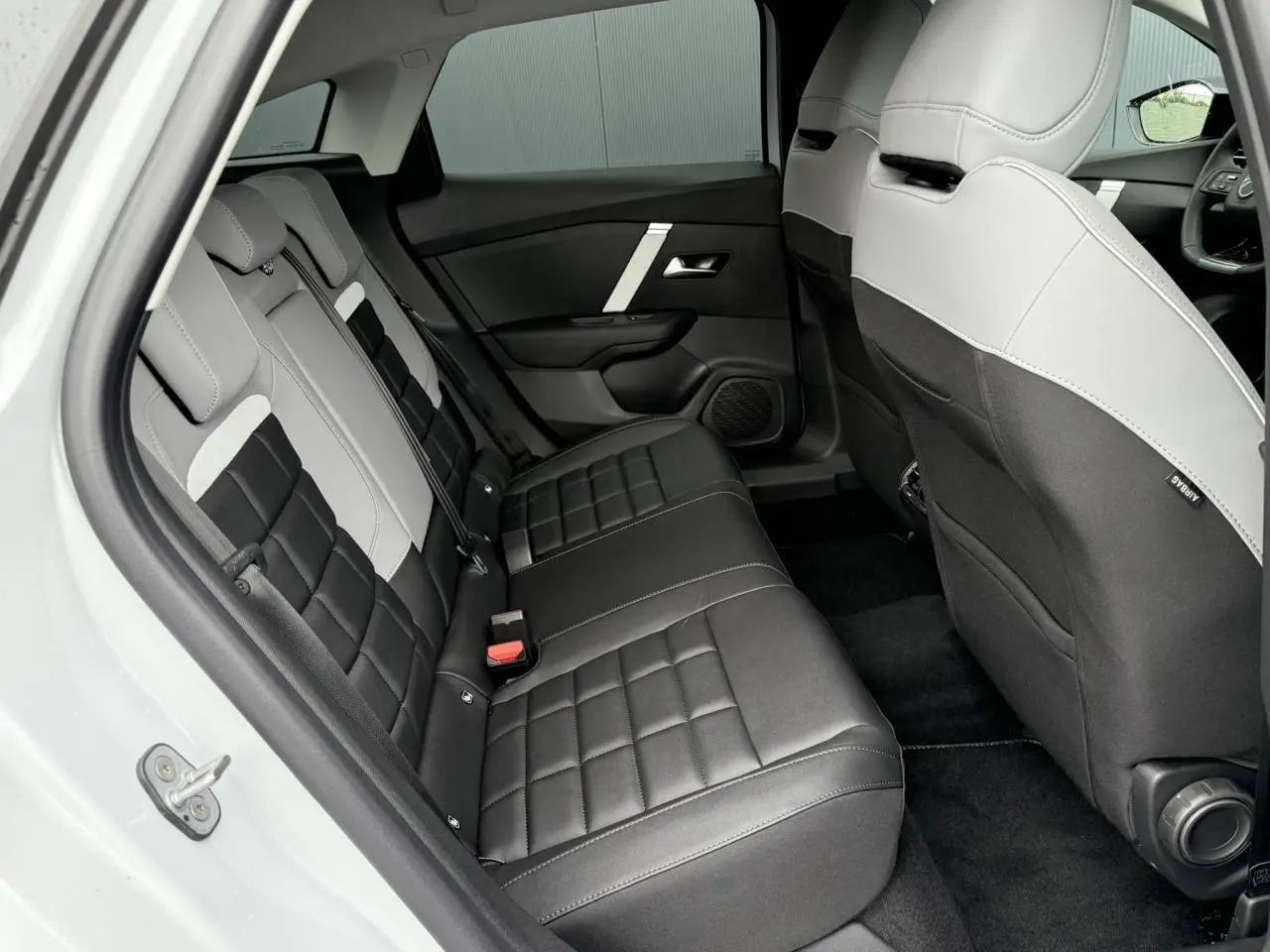 Vue intérieure arrière côté gauche des sièges bicolores noir et gris du Citroën C4 NV Hybrid 2025 avec appuie-têtes intégrés.